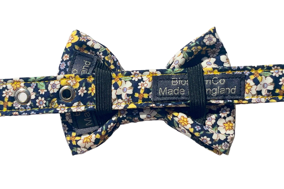Agnes is a handmade fabric bow tie with a navy blue background and a yellow, white, and green floral pattern. Featuring two black elastic band s to attach to any collar. Shown attached to matching Agnes dog collar.