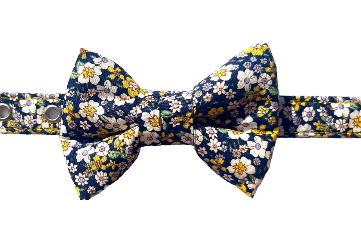 The Agnes bowtie by BlossomCo has a navy blue background with a dense white, yellow, and green floral print. Shown attached to matching Agnes floral print dog collar